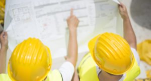 Engineer builders in safety vest with blueprint at construction site